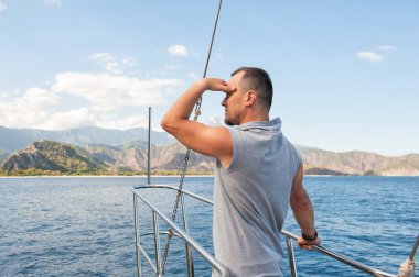 Gezgin adam yatla denize bakıyor dağlık zemin ile okyanus macerasının tadını çıkarıyor.