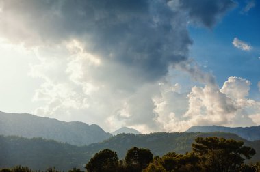 Orman, dağlar ve bulutlu güneşli gökyüzü ile güzel bir atmosfer manzarası.