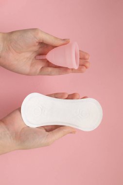 Woman hand making choice between menstrual cup and sanitary pad. Menstruation, period, hygiene concept