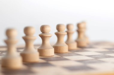 A row of Chess pawns on a wooden chessboard.