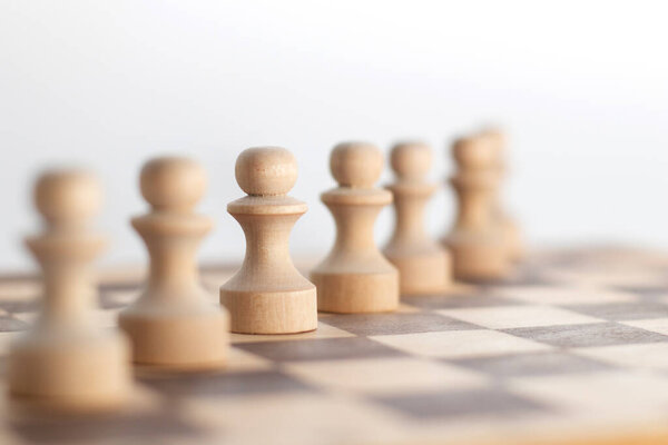 Ряд шахматных пешек на деревянной шахматной доске.