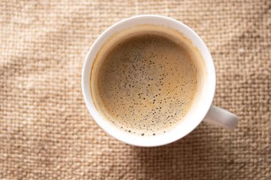 Cup of coffee on brown cloth, top view