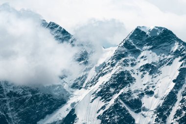 Karla kaplı dağ zirveleri ve beyaz bulutlu gökyüzü. Güzel kış manzarası. 
