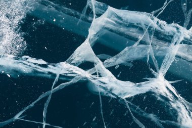 Transparent blue ice with cracks on Baikal lake in winter. Abstract winter nature background.