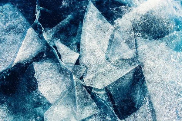 Transparent blue ice with cracks and ice floes on Baikal lake in winter. Abstract winter nature background.