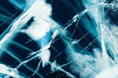 Transparent blue ice with cracks on Baikal lake in winter. Abstract winter nature background.