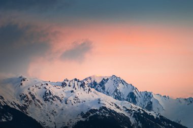 Snow-covered mountains and the pink sky at sunrise. Winter landscape in Alps mountains, France.