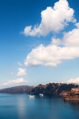 Santorini Adası, Yunanistan. Mavi deniz ve bulutlu mavi gökyüzü. Kıyıya yakın seyir gemileri. Yaz deniz manzarası. Seyahat ve tatil kavramı