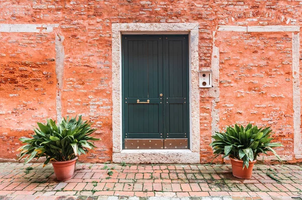 stock image Red brick facade of the house with wooden door and flowers. Old medieval architecture in Venice, Italy.