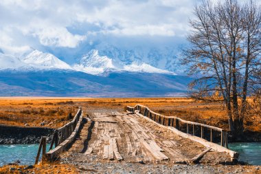 Altai dağlarındaki Chuya Nehri üzerindeki eski ahşap köprü, Sibirya, Rusya. Sonbahar manzarası. Kuzey Chuya sırtı manzarası