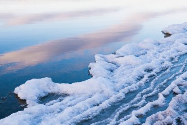 Kışın göl kıyısında buz. Bulutlar ve gökyüzü su yüzeyine yansıyor. Soyut kış doğa arkaplanı.