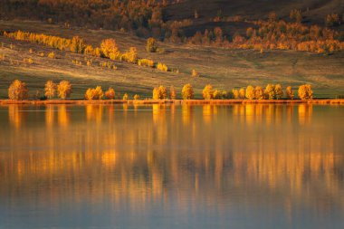 Lake in the autumn mountains. Yellow trees and mountains are reflected in the lake at sunrise. Beautiful autumn landscape.  clipart