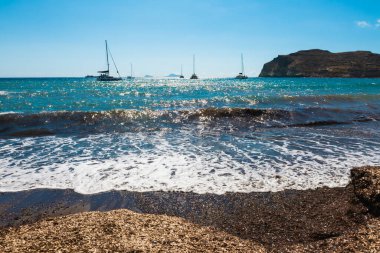 Yunanistan 'ın Santorini adasındaki kırmızı plaj. Yatlar kıyıya yakın seyrediyor. Güneşli bir günde yaz deniz manzarası