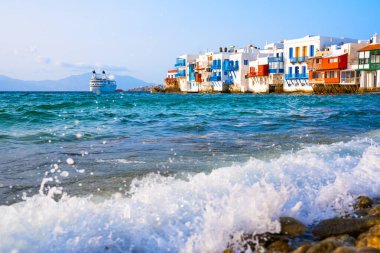 Yunanistan 'ın Mykonos adasındaki Mykonos kasabasının beyaz mimarisi. Adanın yakınındaki bir yolcu gemisinde. Mavi deniz ve mavi gökyüzü gün batımında