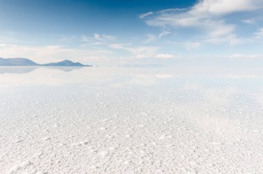 Salar de Uyuni tuz düzlüğü, Altiplano, Bolivya. Bulutlu ve volkanlı mavi gökyüzü su yüzeyine yansıyor. Meşhur seyahat yeri