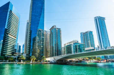 Dubai, Birleşik Arap Emirlikleri - 19 Ocak 2024: Güneşli bir günde modern gökdelenleri ve konut binaları olan Dubai Marina. Güzel gezinti güvertesi ve su kanalının üzerindeki köprü