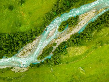 Yeşil ağaçları ve taze yeşil otları olan dağ nehri. Havadan yukarıdan aşağıya doğru. Soyut yaz doğası geçmişi. Kuzey Osetya, Kafkasya, Rusya.