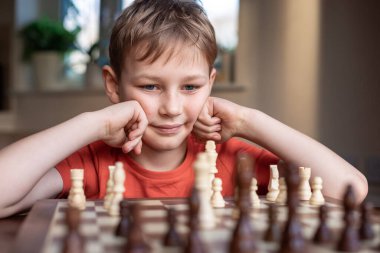 Young white child playing a game of chess on large chess board. Chess board on table in front of school boy thinking of next move, tournament