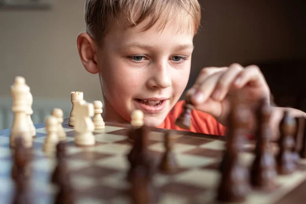 Young white child playing a game of chess on large chess board. Chess board on table in front of school boy thinking of next move, tournament