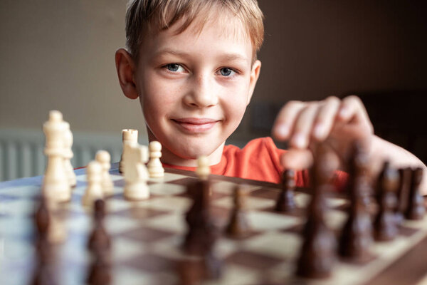Young white child playing a game of chess on large chess board. Chess board on table in front of school boy thinking of next move, tournament