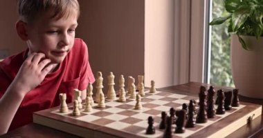 Young white child playing a game of chess on large chess board. Chess board on table in front of school boy thinking of next move, tournament