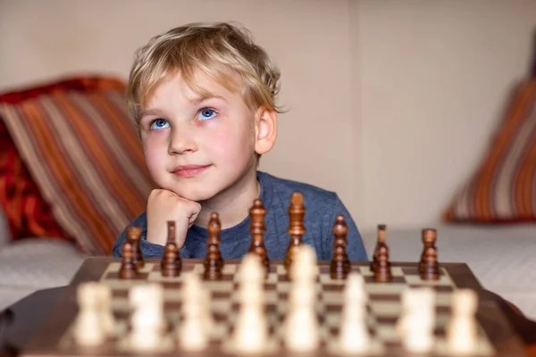 Small child 5 years old playing a game of chess on large chess board. Chess board on table in front of the boy thinking of next move, tournament