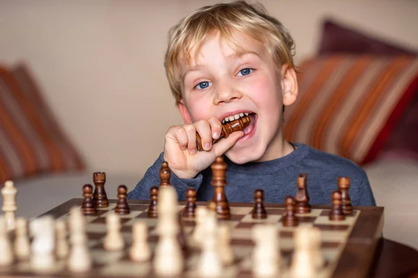 5岁的小孩在大棋盘上玩国际象棋 棋盘放在男孩面前的桌子上 高高兴兴地吃着丢失的一块 — 图库照片