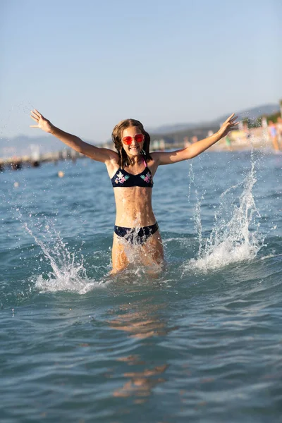 海のビーチで楽しい時間を過ごしているピンクのサングラスの10代の女の子は 波とスプラッシュで遊んでいます 夏休みのコンセプトで楽しい — ストック写真