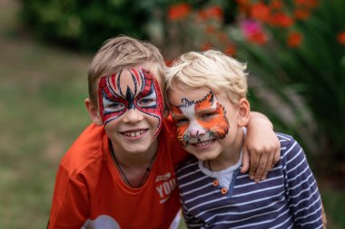 Yüzleri boyanmış iki küçük mutlu çocuk. Yüz boyama, doğum günü partisinde ya da tatillerde yüzleri boyayan çocuklar.