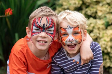 Yüzleri boyanmış iki küçük mutlu çocuk. Yüz boyama, doğum günü partisinde ya da tatillerde yüzleri boyayan çocuklar.