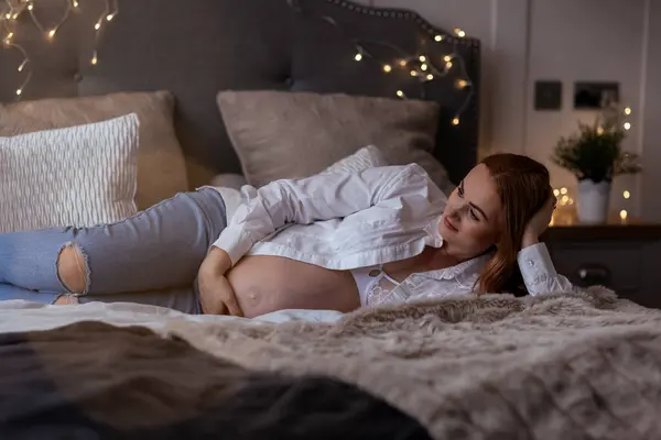 漂亮的红头发中年孕妇在家里的床上等着孩子 图库图片
