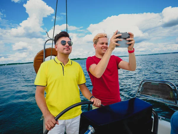 two persons sailing on a sailing yacht, one guy steering wheel and other steering with drone. summer vacations on yacht