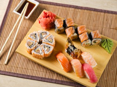 Suşi soslu, somon, yılan balığı, ton balığı ve karidesli wasabi ve zencefille süslenmiş ahşap bir tahta üzerinde.
