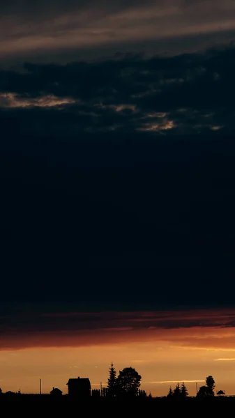 Gün batımında bir ev ve ağaçların siluetleri.