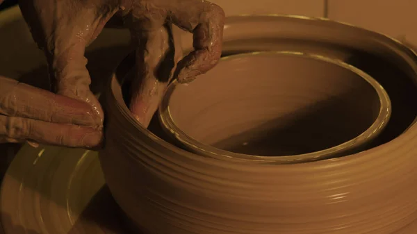 Hands mold a vase of clay