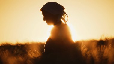 Gün batımında buğday tarlasında yaşlı bir kadının silueti.