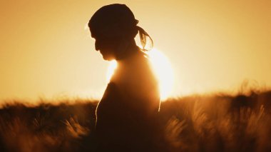 Gün batımında buğday tarlasında yaşlı bir kadının silueti.