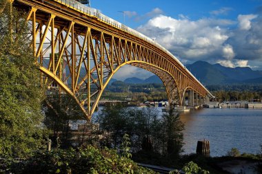 A transport bridge with a yellow metal frame  across in a narrow place in the bay against the backdrop of a mountain range and a cloudy sky