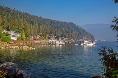 Kuzey Vancouver 'daki Deep Cove' da sahil köyü ve marina, dağ sırasının ve mavi gökyüzünün arka planında marinada yelken açmak. Vancouver, British Columbia, Kanada
