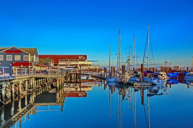 Steveston köyündeki gezinti alanı, Richmond City 'nin rıhtımındaki balıkçı marinası ve restoranların yaz sahaları mavi gökyüzünün arka planında.
