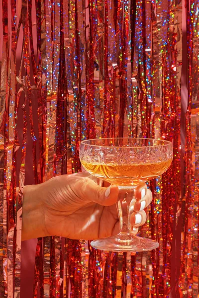 A glass of champagne in a woman's hand on the background of a festive New Year's party background.