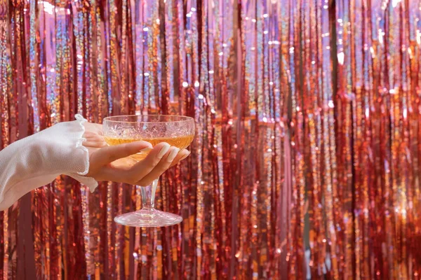A glass of champagne in a woman\'s hand on the background of a festive New Year\'s party background.