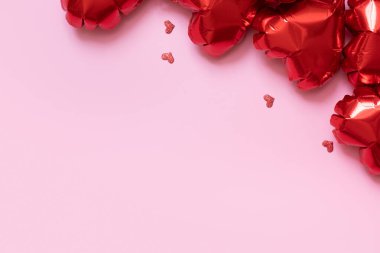 Red heart shape foil balloons on pink background. Valentines Day background with copy space.