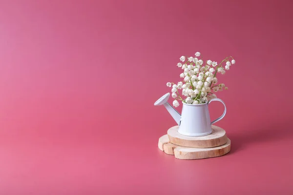 Spring, Mother's Day or March 8 still life composition with lilies of the valley bouquet in a decorative watering can on a magenta background