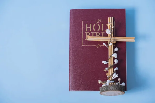 Holy Bible with cross and decorative flowers on blue background.