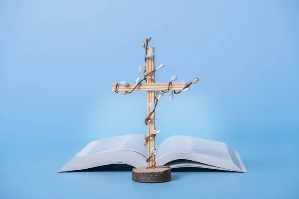 Cross decorated flowers with Holy Bible on blue background. Easter holiday minimalistic concept.