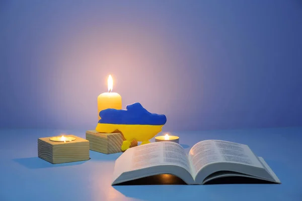 Ukraine map and Holy Bible with candles lighting on colored background