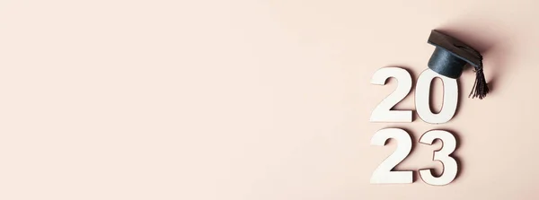 Banner with Wooden number 2023 with graduated cap on beige background. Class of 2023 concept.