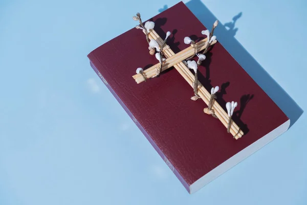 Cross decorated flowers with Holy Bible on blue background. Easter holiday minimalistic concept.
