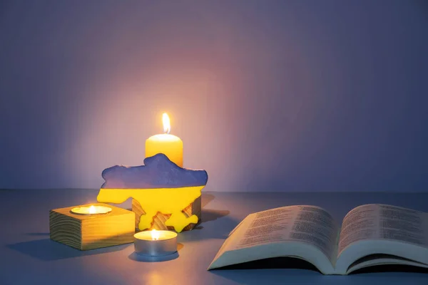 Ukraine map and Holy Bible with candle lighting on colored background. Pray for Ukraine concept.